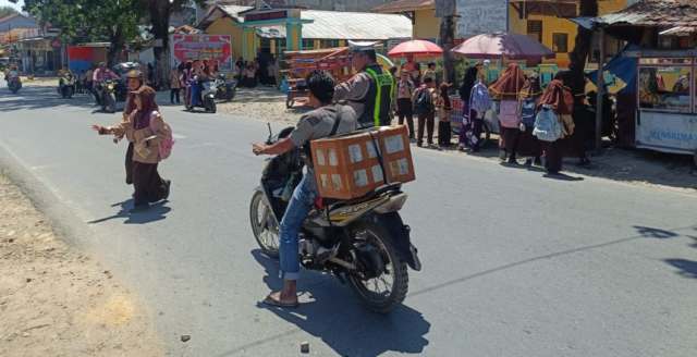 Kapos Lantas Polsek Barumun, Aipda Irfan Aulia Lubis, melakukan pengaturan arus lalu lintas disaat pelajar SD  keluar sekolah.